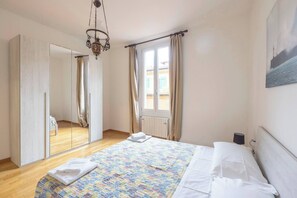 A bedroom with a bed, a mirror, a window with curtains, a radiator, and a hanging light fixture. - Family & Friends (Bologna)