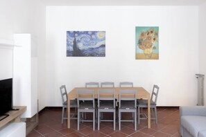 A dining area with a table and chairs, a television, and two paintings on the wall.