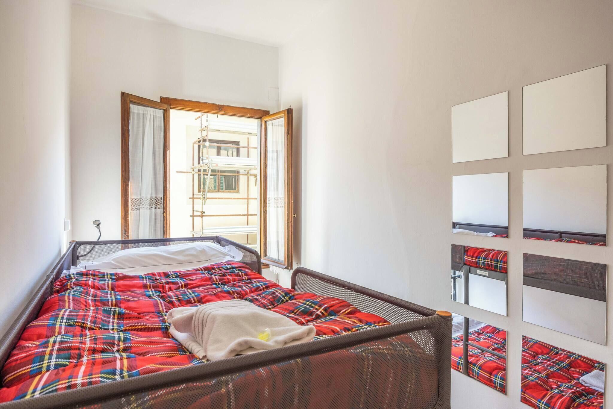 A single bed with a plaid blanket, a window with curtains, and a wall with framed pictures.
