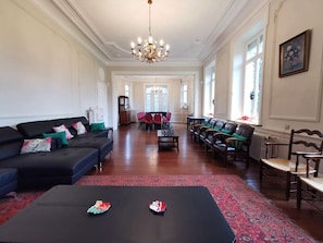 Ein geräumiges Wohnzimmer mit einer schwarzen Couch, roten und grünen Sesseln, einem Couchtisch und einer Pendelleuchte.
