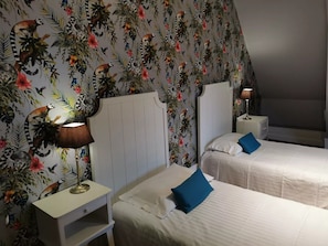 Ein Hotelzimmer mit zwei Betten, einem Nachttisch mit Lampe und einer Wand mit Dschungel-Muster-Tapete.