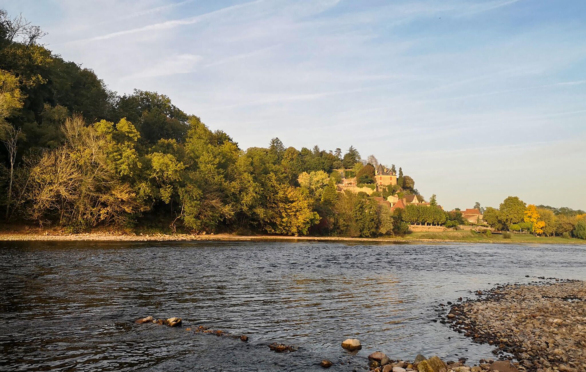 A river with a rocky shoreline and a forested hillside in the background.