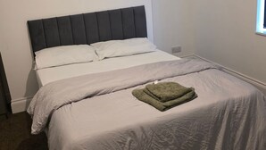A bedroom with a bed, white bedding, a grey headboard, and a window.