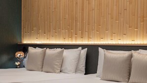 Een net opgemaakt bed met witte lakens en meerdere kussens, een muur met verticale houten latten, en een klein tafeltje met een lamp en decoratie.