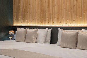 A neatly made bed with white linens and multiple pillows, a wall with vertical wooden slats, and a small table with a lamp and decorative item. - JAPAVISTA Maverique (KONOHANA WARD)