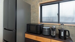 Een keuken met een koelkast, magnetron, koffiezetapparaat en waterkoker op een houten aanrecht.