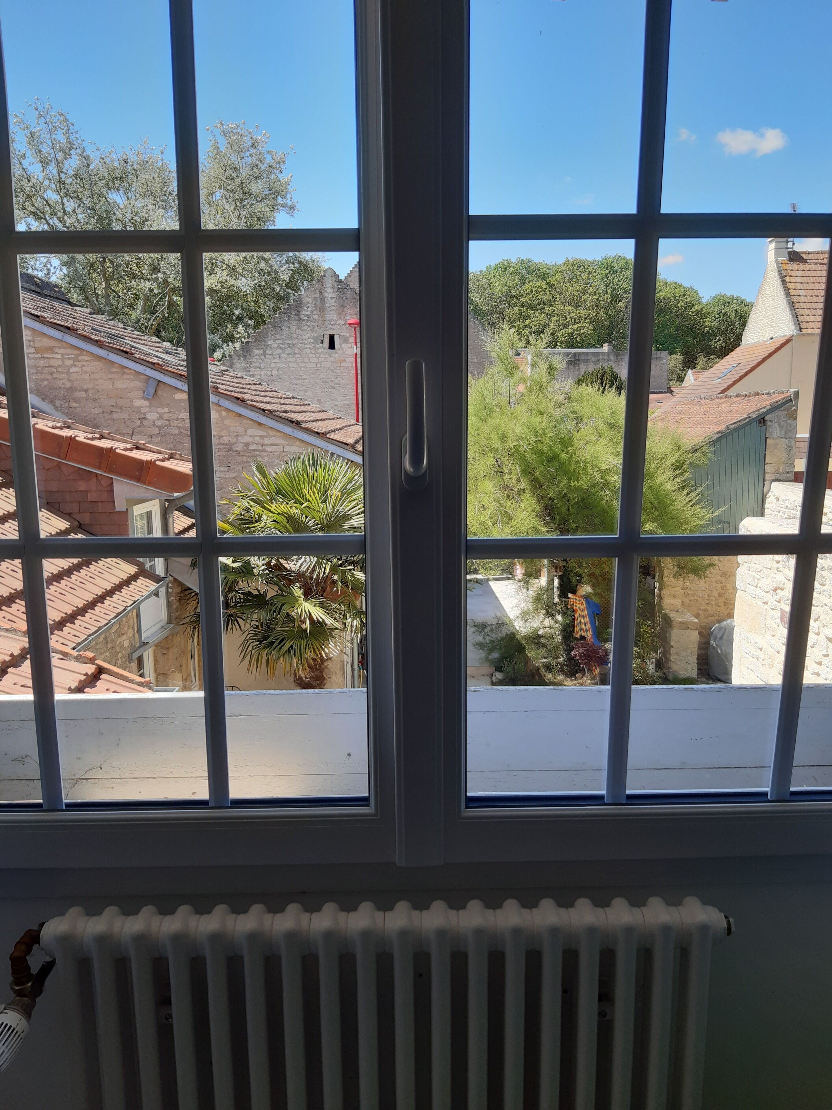 A window with a view of a building with a tiled roof, a stone wall, and some greenery.