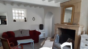 Un salon avec un canapé rouge, des fauteuils blancs, une petite table, une cheminée et un miroir.