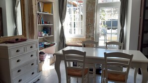 Une pièce comprenant une table blanche, quatre chaises, une commode blanche avec des tiroirs, une bibliothèque et un grand miroir.