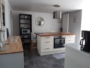 A modern kitchen with white cabinetry, a wooden countertop, a built-in microwave, and a coffee machine.