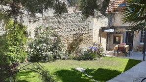 Un bâtiment en pierre avec un mur en pierre, une pelouse verdoyante et une terrasse avec une table et des chaises.
