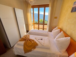 A hotel room with a bed, a view of mountains through a window, and a balcony. - Marcus 706 Apartment, Residence with Pool and Lake View (Tignale)