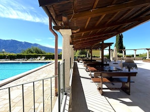 A poolside area with a covered seating area, stone flooring, and a view of mountains in the background. - Marcus 706 Apartment, Residence with Pool and Lake View (Tignale)