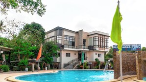 Zona de piscina con un edificio al fondo, una bandera y un cartel que indica la profundidad de la piscina.
