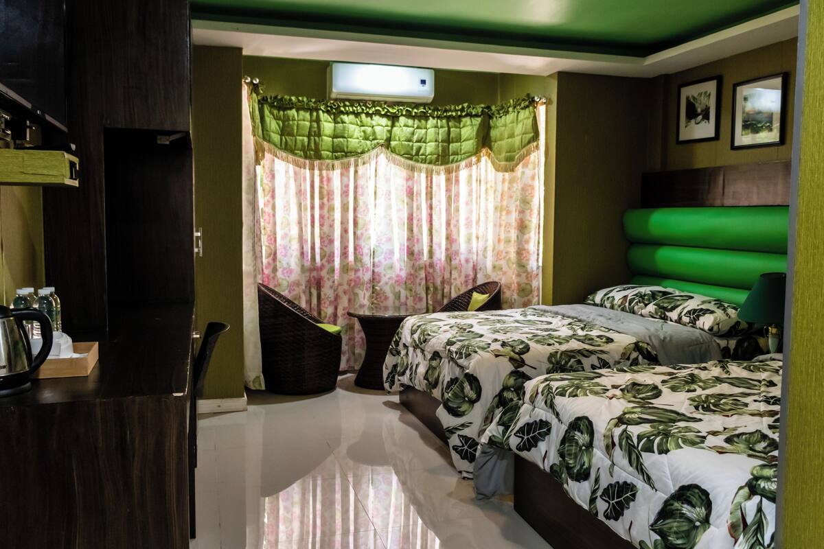Un dormitorio con cama, escritorio, silla, mesita y ventana con cortinas.