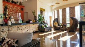 Un hall de hotel con mostrador de recepción, zona de estar, estatuas decorativas y un amplio ventanal que proporciona luz natural.