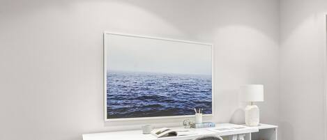 A white desk with a framed picture of the ocean, a lamp, and a chair.