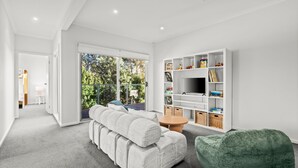 Una sala de estar moderna con un sofá, un reposapiés verde, un televisor y una estantería.