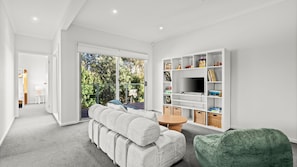A modern living room with a sofa, a green ottoman, a TV, and a bookshelf. - Dunehaven - Point Lonsdale (Point Lonsdale)