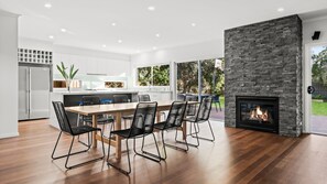 A modern kitchen with a dining area, a stone fireplace, and a large window. - Dunehaven - Point Lonsdale (Point Lonsdale)