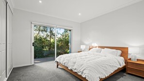 A bedroom with a bed, nightstands, a door leading to a balcony, and a view of trees. - Dunehaven - Point Lonsdale (Point Lonsdale)