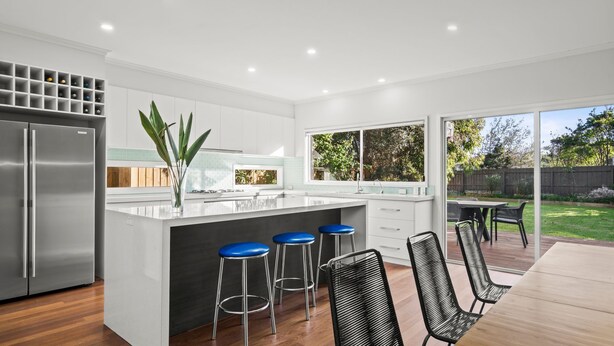 Una cocina moderna con una isla central, taburetes de bar y un comedor con sillas.