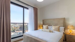 Un dormitorio con una cama grande, dos mesitas de noche, un ventanal con cortinas y vistas a la ciudad.