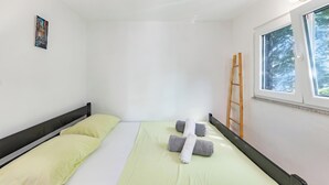 A single bed with two pillows, a window with a view of trees, and a ladder leaning against the wall. - Pool & Garden House Jaga (Polaca)
