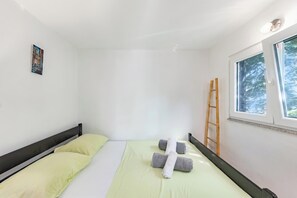 A single bed with two pillows, a window with a view of trees, and a ladder leaning against the wall. - Pool & Garden House Jaga (Polaca)