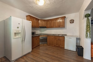 A kitchen with wooden cabinets, a white refrigerator, a microwave, an oven, and a dishwasher. - Pool & Garden House Jaga (Polaca)