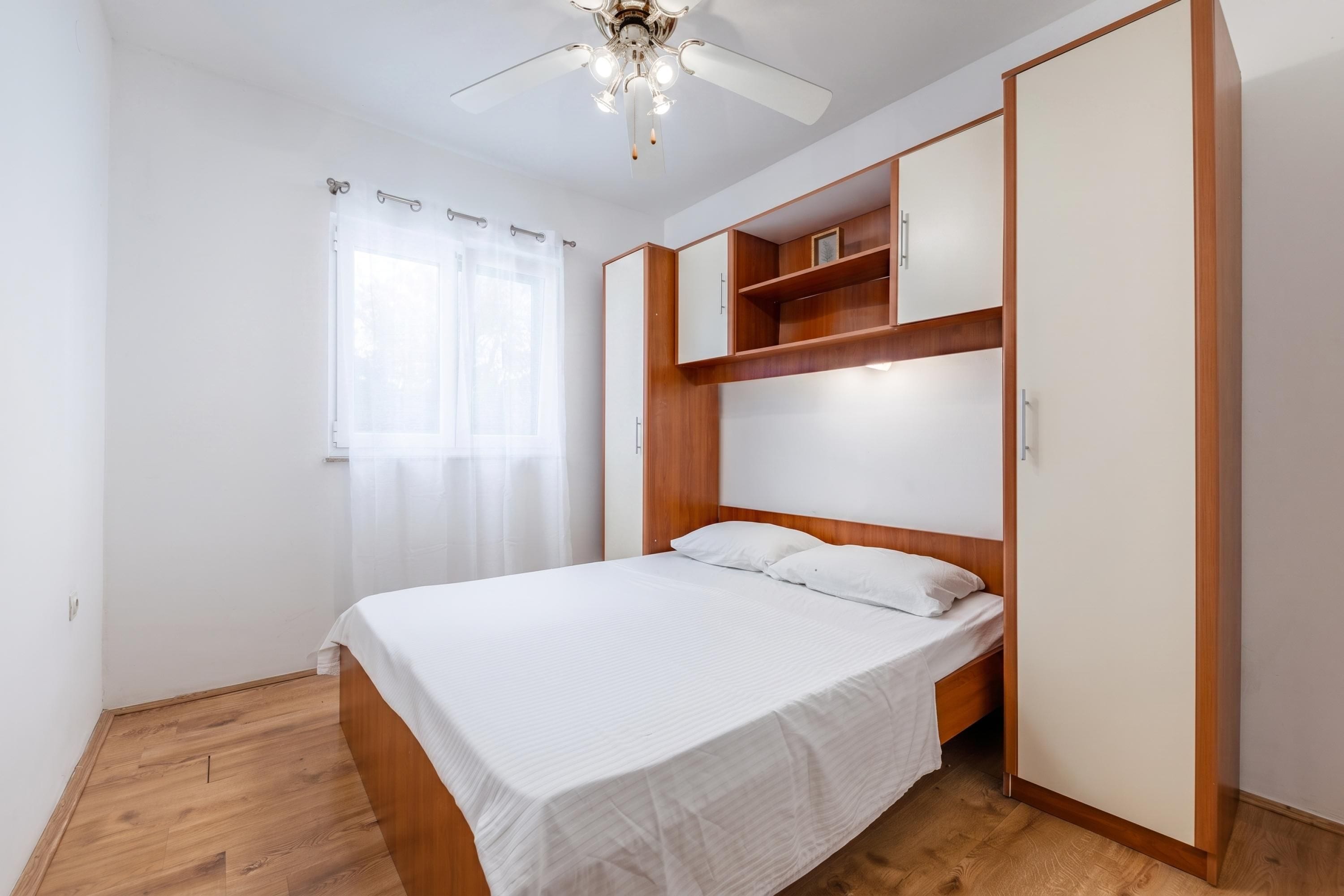 A bedroom with a bed, a wardrobe, a ceiling fan, and a window with curtains.