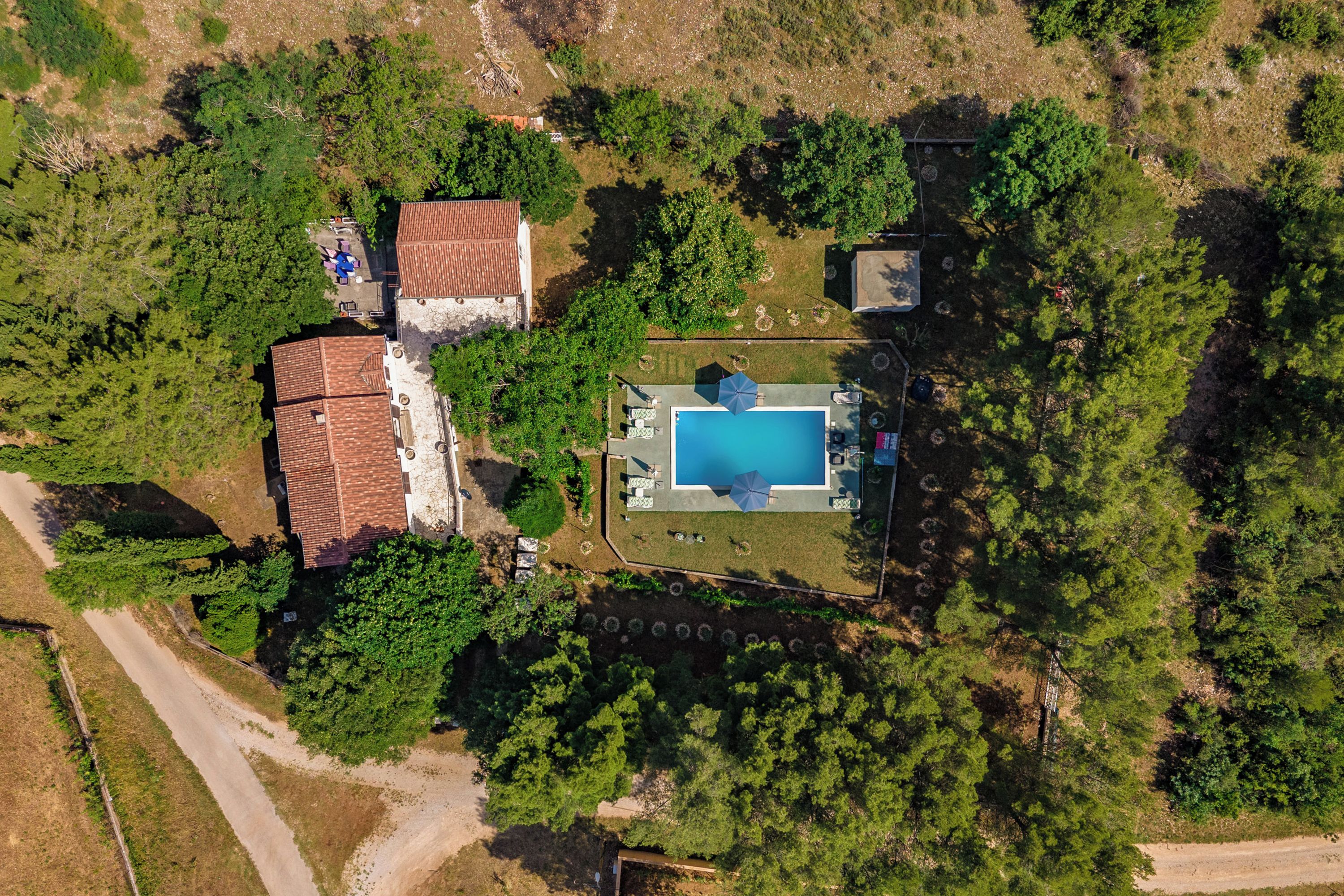 An aerial view of a property with a swimming pool, a fenced yard, and a building with a red roof.