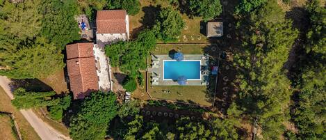An aerial view of a property with a swimming pool, a fenced yard, and a building with a red roof.