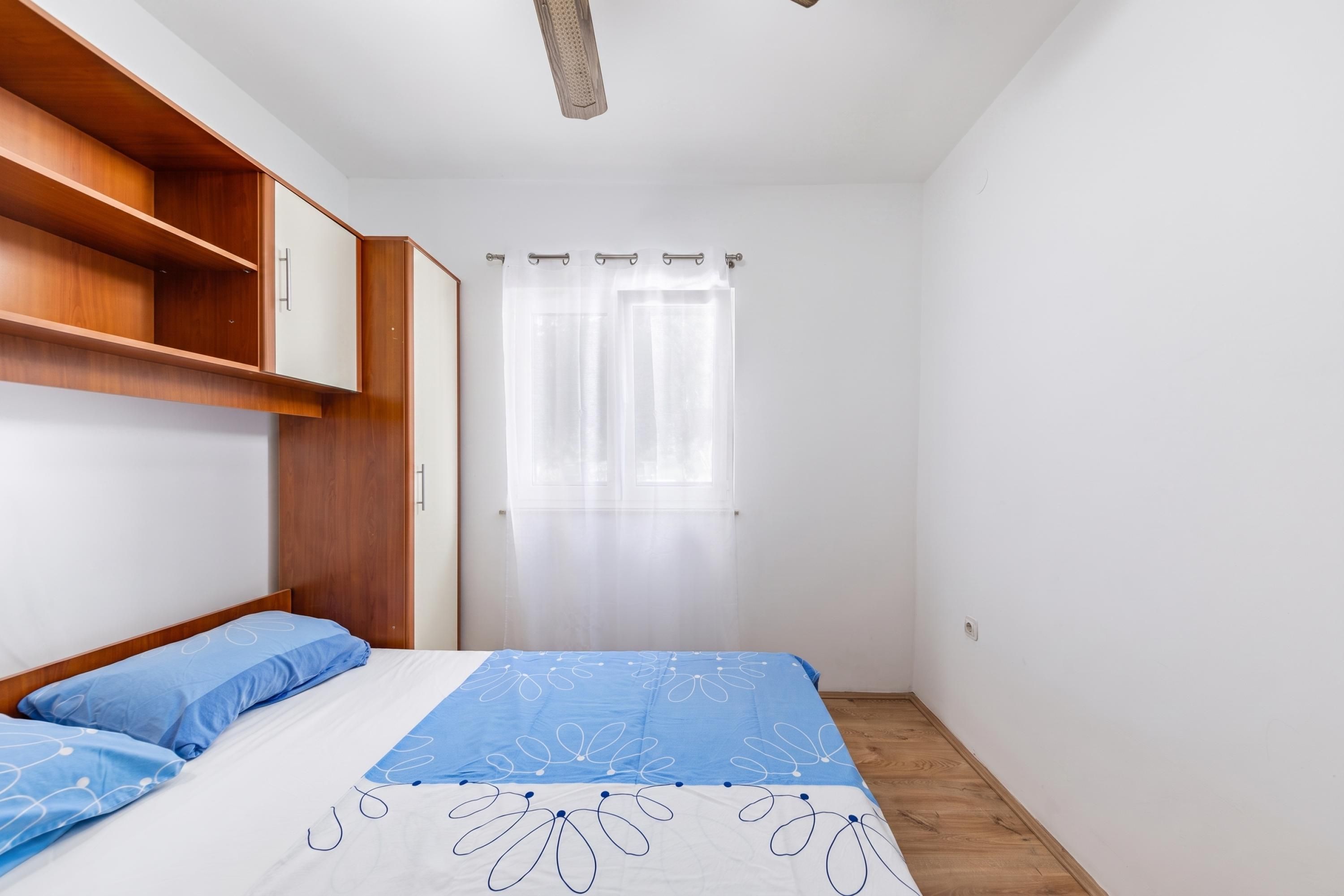 A bedroom with a bed, a wardrobe, a window with curtains, and a ceiling fan.