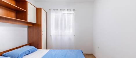 Un dormitorio con cama, armario, ventana con cortinas y ventilador de techo.