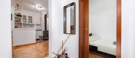 A bedroom with a wooden door, a bed with white bedding, and a small bedside table.
