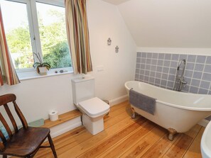 Ein Badezimmer mit Toilette, Badewanne, Holzboden, einem Fenster mit Vorhängen und einer Topfpflanze.