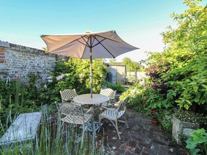 Eine Terrasse mit rundem Tisch, Stühlen, einem Sonnenschirm und einer Ziegelwand.