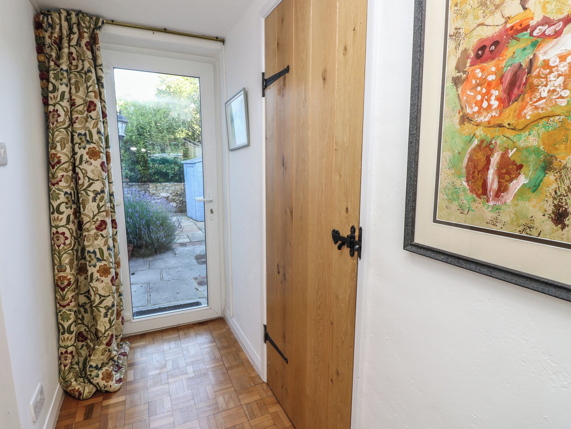 A hallway with a wooden door, a patterned curtain, and a framed painting on the wall.