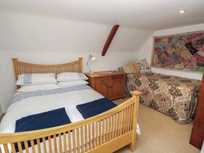 A bedroom with a wooden bed, a nightstand, a lamp, a patterned wall hanging, and a carpeted floor. - 5 Castle Street (Newport)