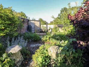 Ein Garten mit einem Ziegelweg, einer Holzkonstruktion und verschiedenen Pflanzen.