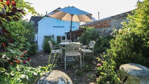A house with a blue exterior, a brick wall, and a garden with a table and chairs under a large umbrella. - 5 Castle Street (Newport)