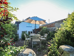 Ein Haus mit blauer Fassade, einer Ziegelwand und einem Garten mit Tisch und Stühlen unter einem großen Sonnenschirm.