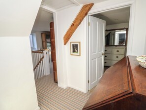 A hallway with a wooden staircase, a white door, and a dresser with a mirror. - 5 Castle Street (Newport)