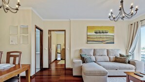 A living room with a sofa, a dining table, and a chandelier. - Our Nest - Where Light and Tranquility Meet (Caniço)