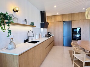 A modern kitchen with a central island, wooden cabinets, a built-in oven, and a dining area with a table and chairs.