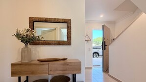 Un pasillo con una consola de madera, cestas de mimbre, un florero con flores y un espejo en la pared.
