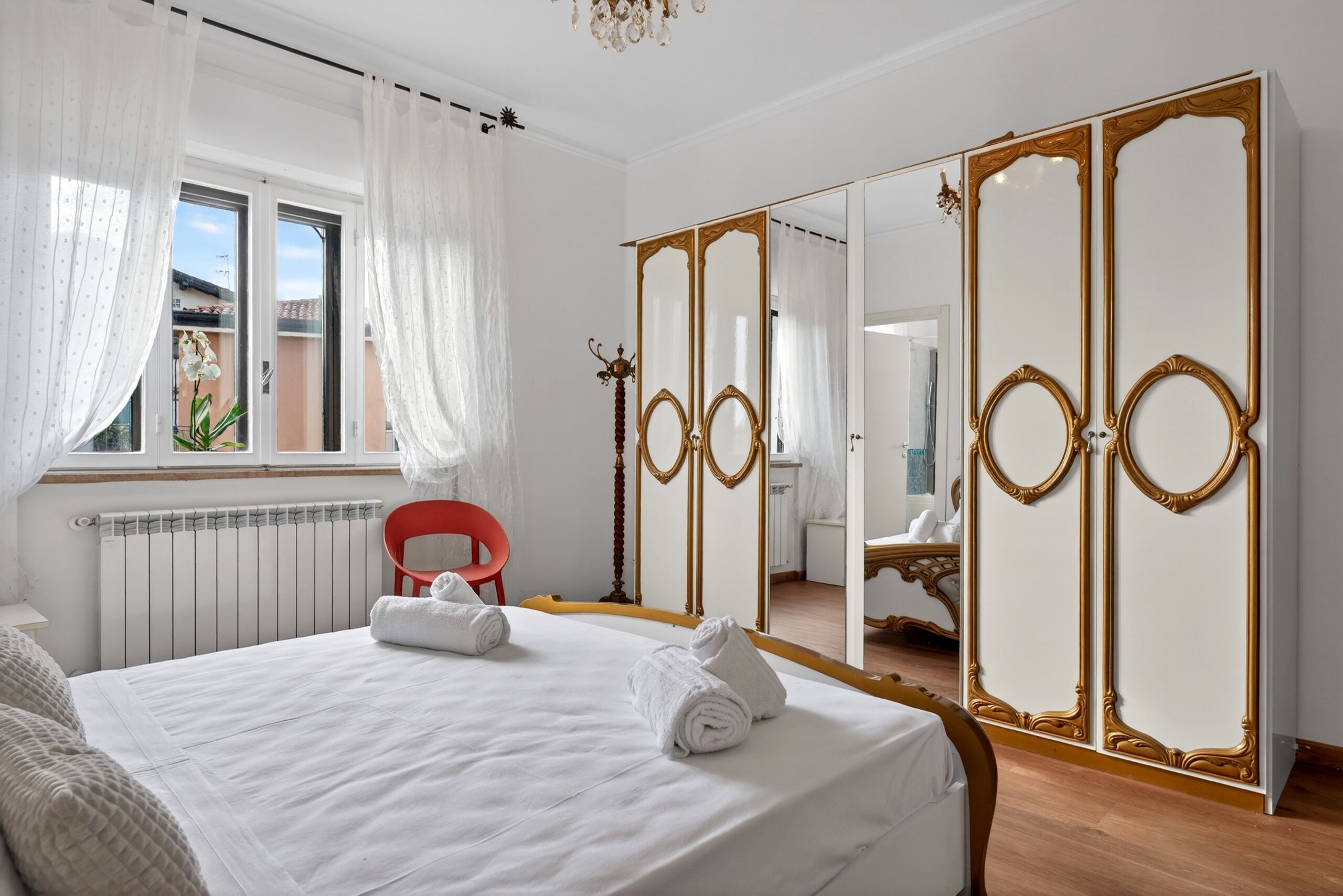 Camera d'albergo con un letto, una poltrona rossa, un armadio con specchi e vista sull'esterno.