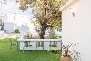 Eine Terrasse mit einer weißen Mauer, einem großen Baum und drei grünen Stühlen.