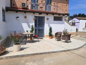 A patio area with a round table and chairs, potted plants, and a building with a brick facade and a blue door. - The Open Space Barn (Calabria)